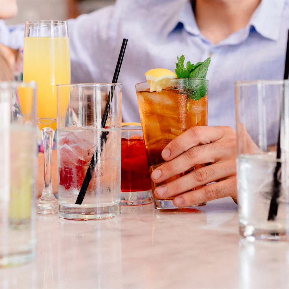 A person holding a soda with ice, with several other soda cups on the table