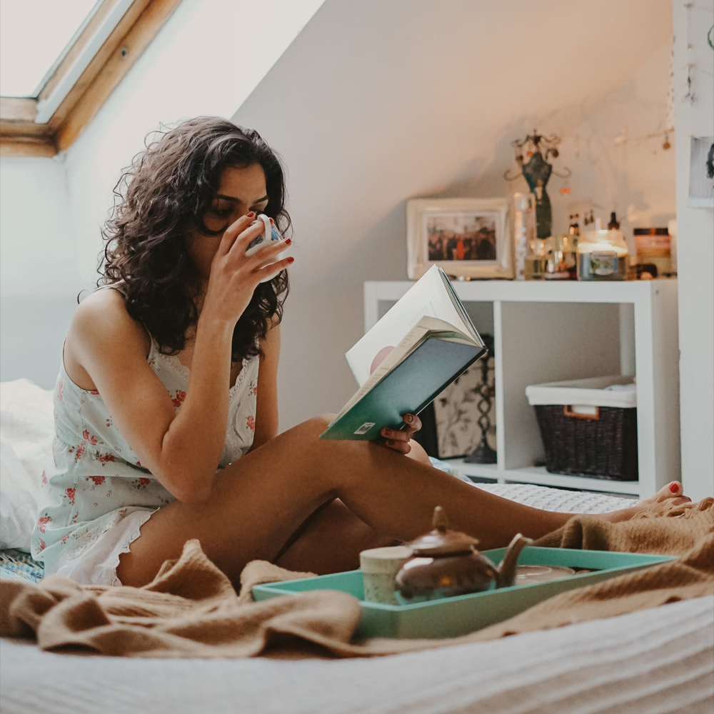 A woman sitting in a cozy room, sipping tea while reading a book