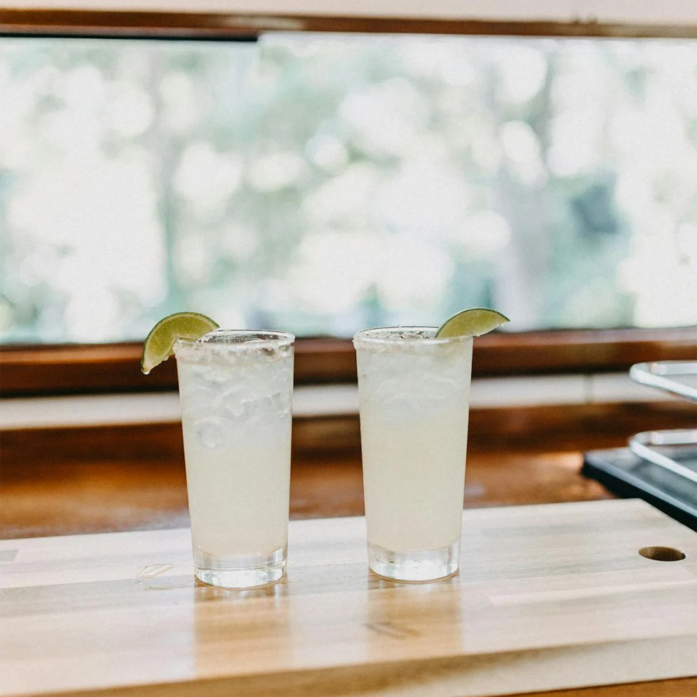 Two glasses of sparkling water with ice cubes on a table with a window background, perfect for sharing.