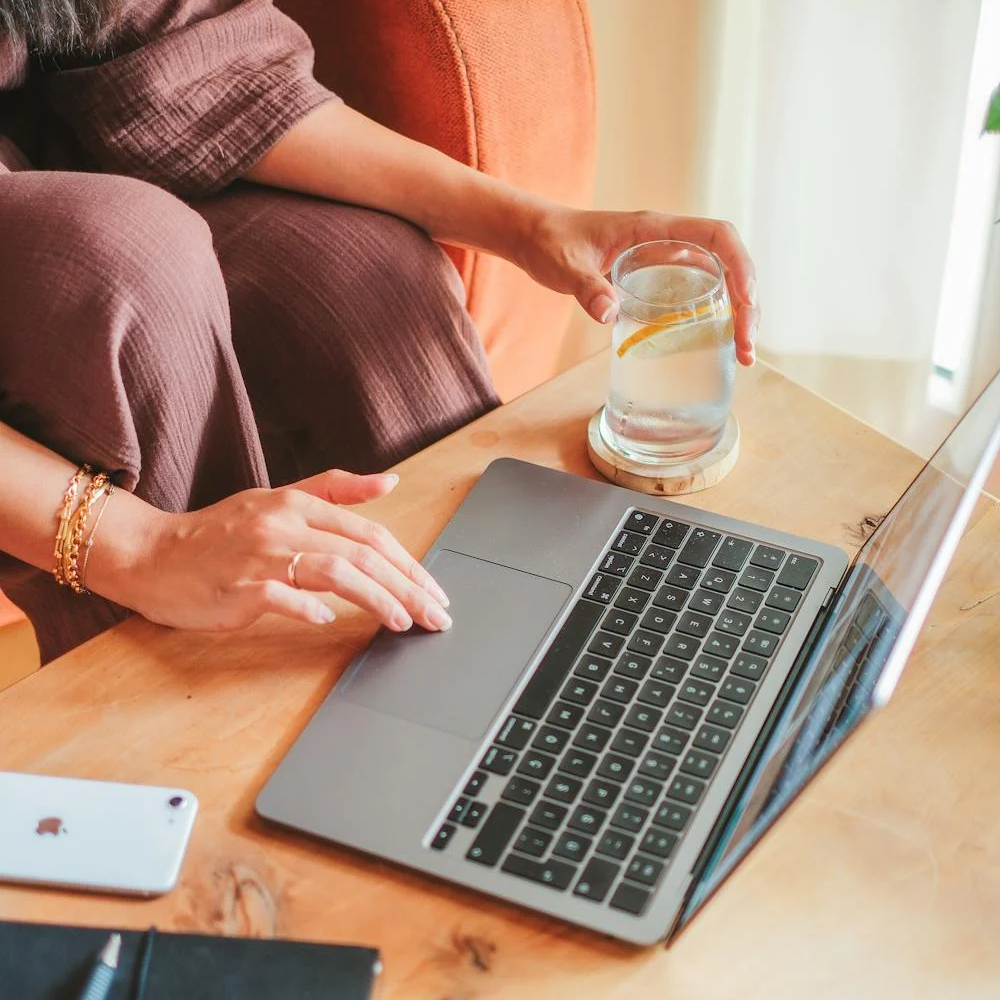 Person holding a glass of soda water with lemon slice while working on a laptop